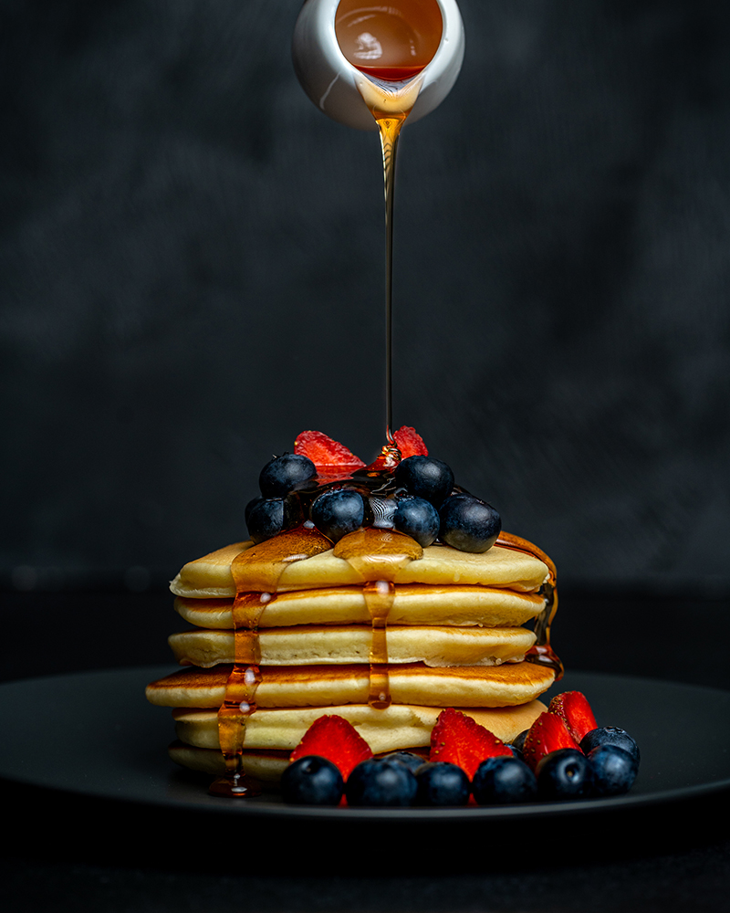 Pouring honey over a stack of delicious blueberry and strawberry pancake dessert. PIXERF