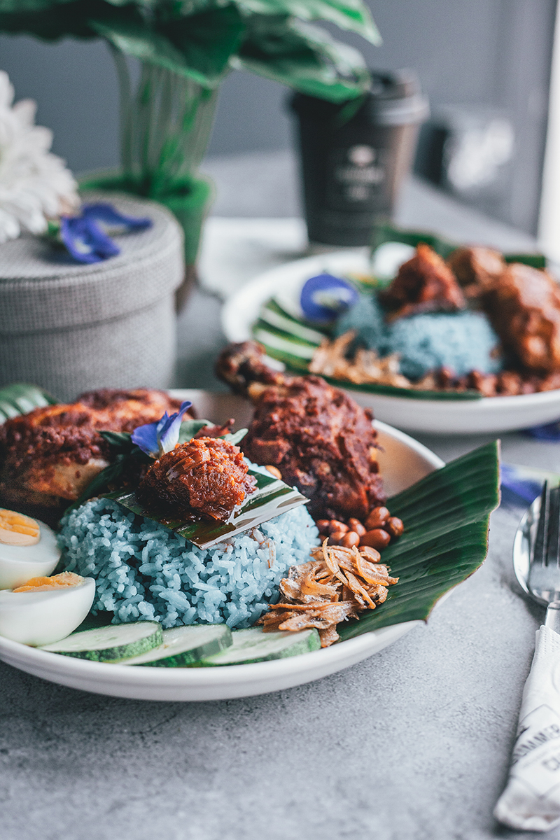 Taditional Nasi Lemak with chicken wings and drumsticks, egg, fried anchovies (ikan bilis) and chilli served in white ceramic plates. PIXERF.