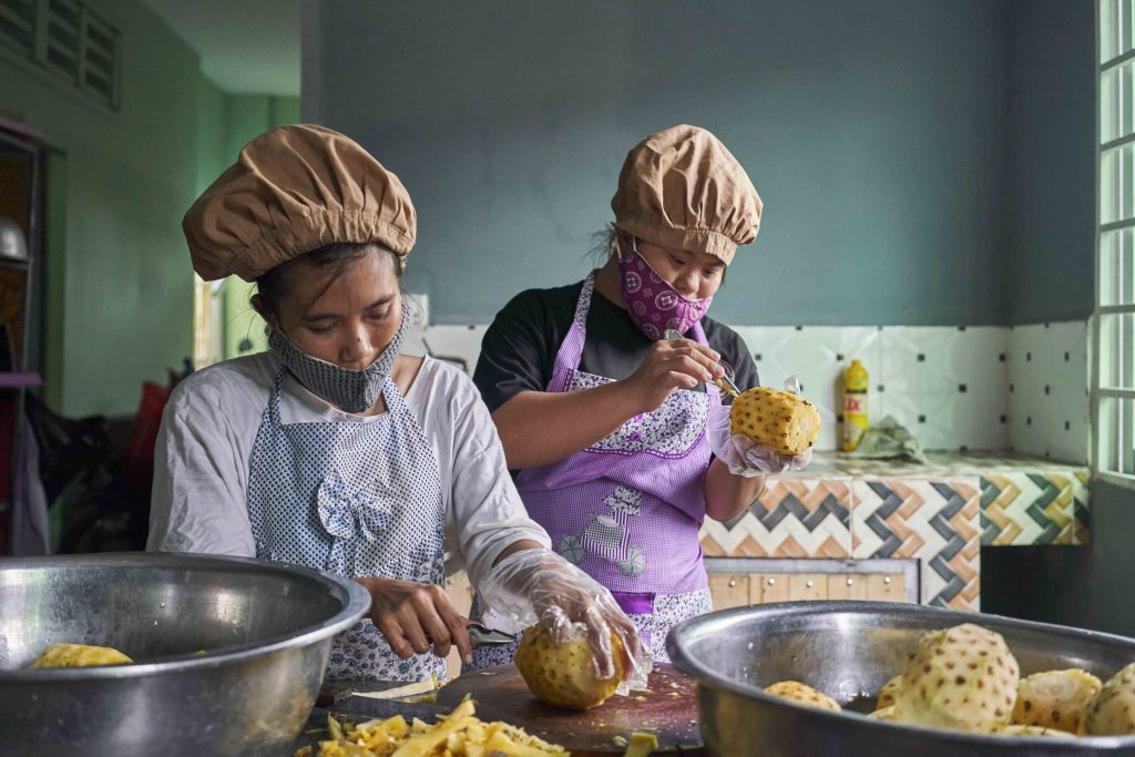 Two women cutting pineapples in a kitchen